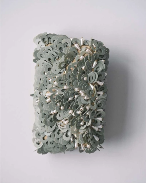 Abstract wall art featuring circular paper discs and droplet-shaped beads, creating a textured and unique decorative piece on white wall.