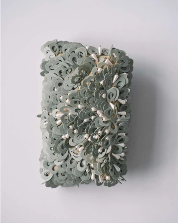 Abstract wall art featuring circular paper discs and droplet-shaped beads, creating a textured and unique decorative piece on white wall.