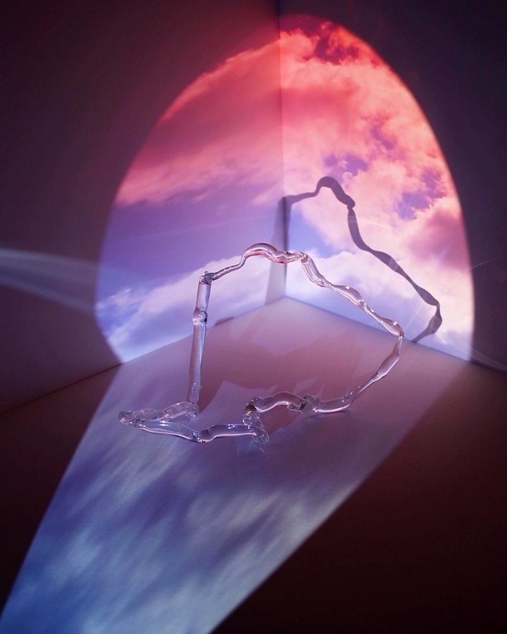 Abstract image with a wavy clear glass object reflecting a blue and pink sky against a white corner surface, showcasing light and shadow.