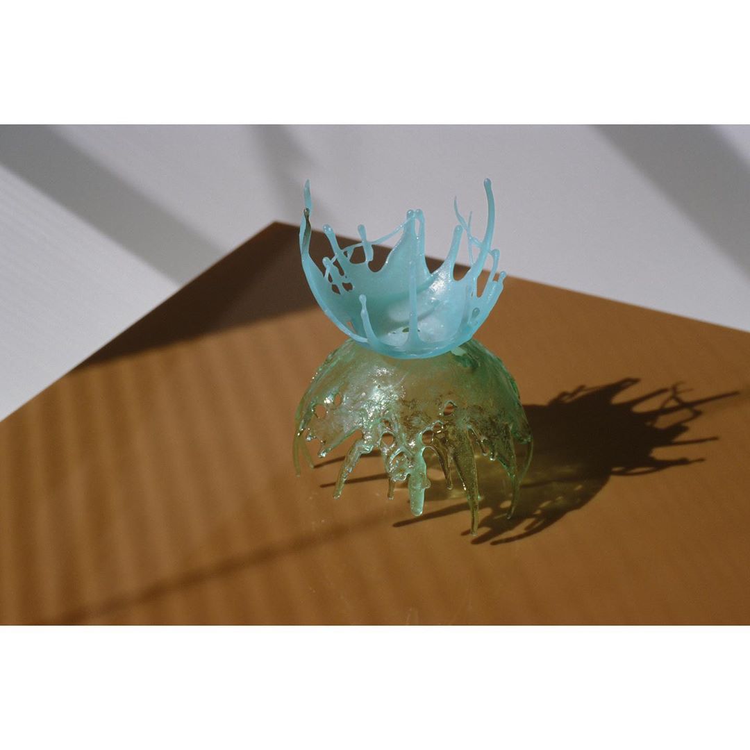Studio shot of two decorative clear plastic sculptures, one light green and one light blue, on a brown surface with a white background.