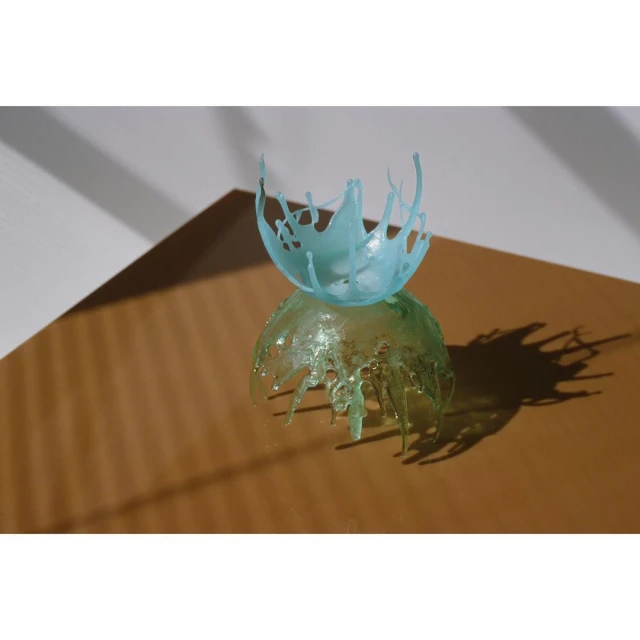 Studio shot of two decorative clear plastic sculptures, one light green and one light blue, on a brown surface with a white background.