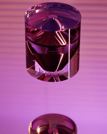 Elevated view of a crystal cosmetic jar with the La Prairie logo, displaying shiny reflections against a soft pink gradient backdrop.