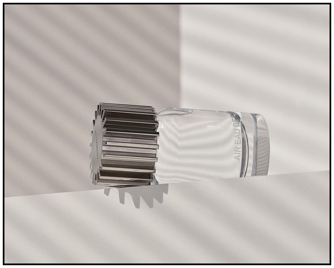 Crystal perfume bottle with a metallic cap, showcased on a clean white surface against a backdrop of soft, linear light patterns.