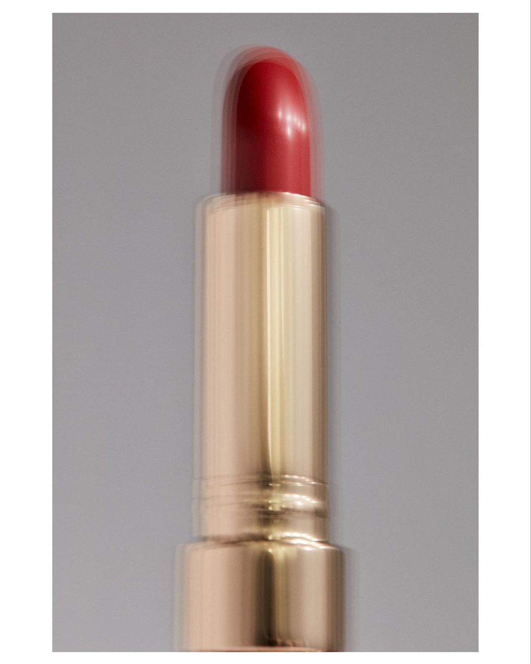 Close-up of red lipstick with gold tube on grey backdrop, showcasing beauty product, makeup and cosmetic photography with studio lighting.