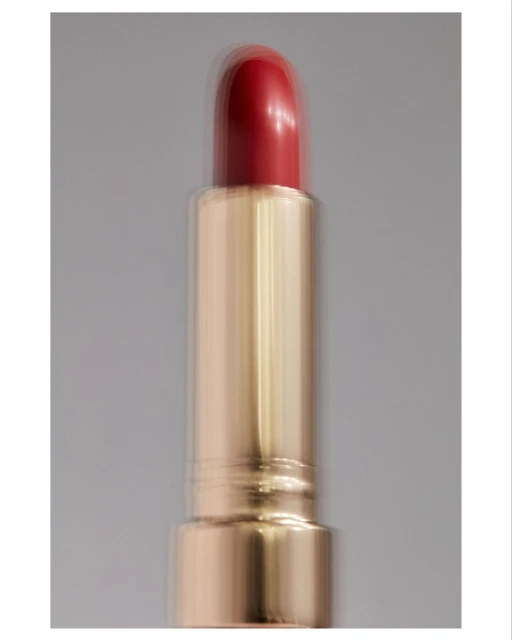Close-up of red lipstick with gold tube on grey backdrop, showcasing beauty product, makeup and cosmetic photography with studio lighting.