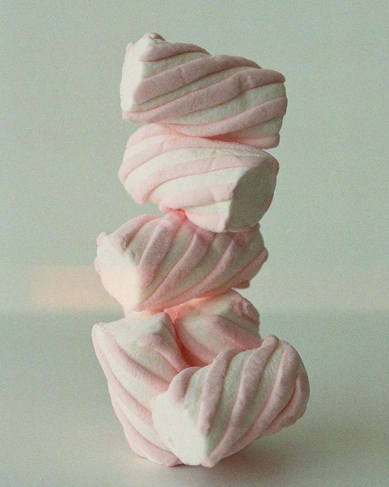 A stack of marshmallows with pink stripes dominates a simple still-life image, set against a light grey background, showcasing textures.