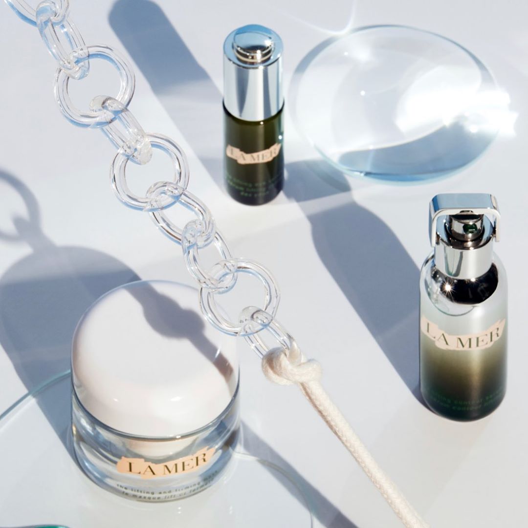 La Mer skincare product still life featuring a cream jar, serum, and lotion against a white background with a clear chain.