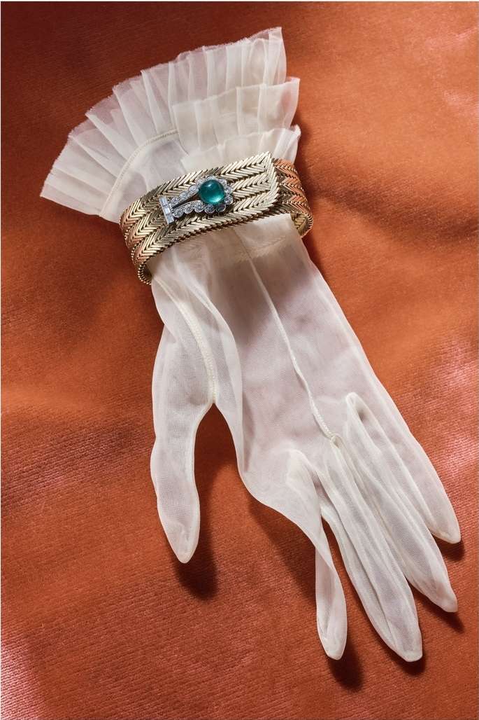 Elegant sheer glove with a ruffled cuff and a vintage gold bracelet with green gem displayed on a textured orange surface.