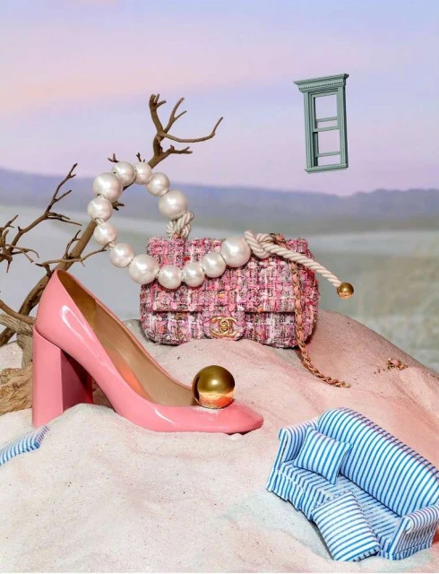 Fashion still life featuring a pink Chanel handbag, pink patent leather high heel, a miniature striped couch, and a window frame prop.