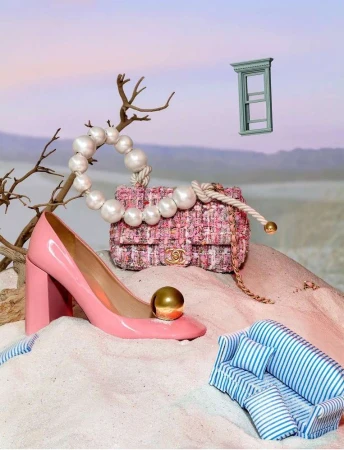Fashion still life featuring a pink Chanel handbag, pink patent leather high heel, a miniature striped couch, and a window frame prop.