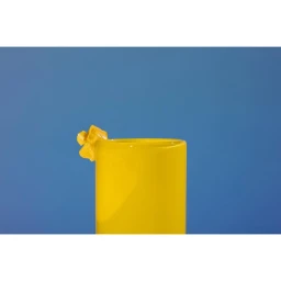 Bright yellow ceramic cup against a solid blue background with a yellow crystallized mineral attached to the rim.