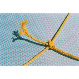 Close-up of a knotted yellow rope with a frayed end resting against a blue patterned background, photographed by Lauren Coleman.