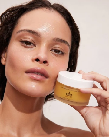 Woman with glowing skin holds ALO brand skincare. Studio close-up of beauty product in hand, product focus, beauty and skincare concept.