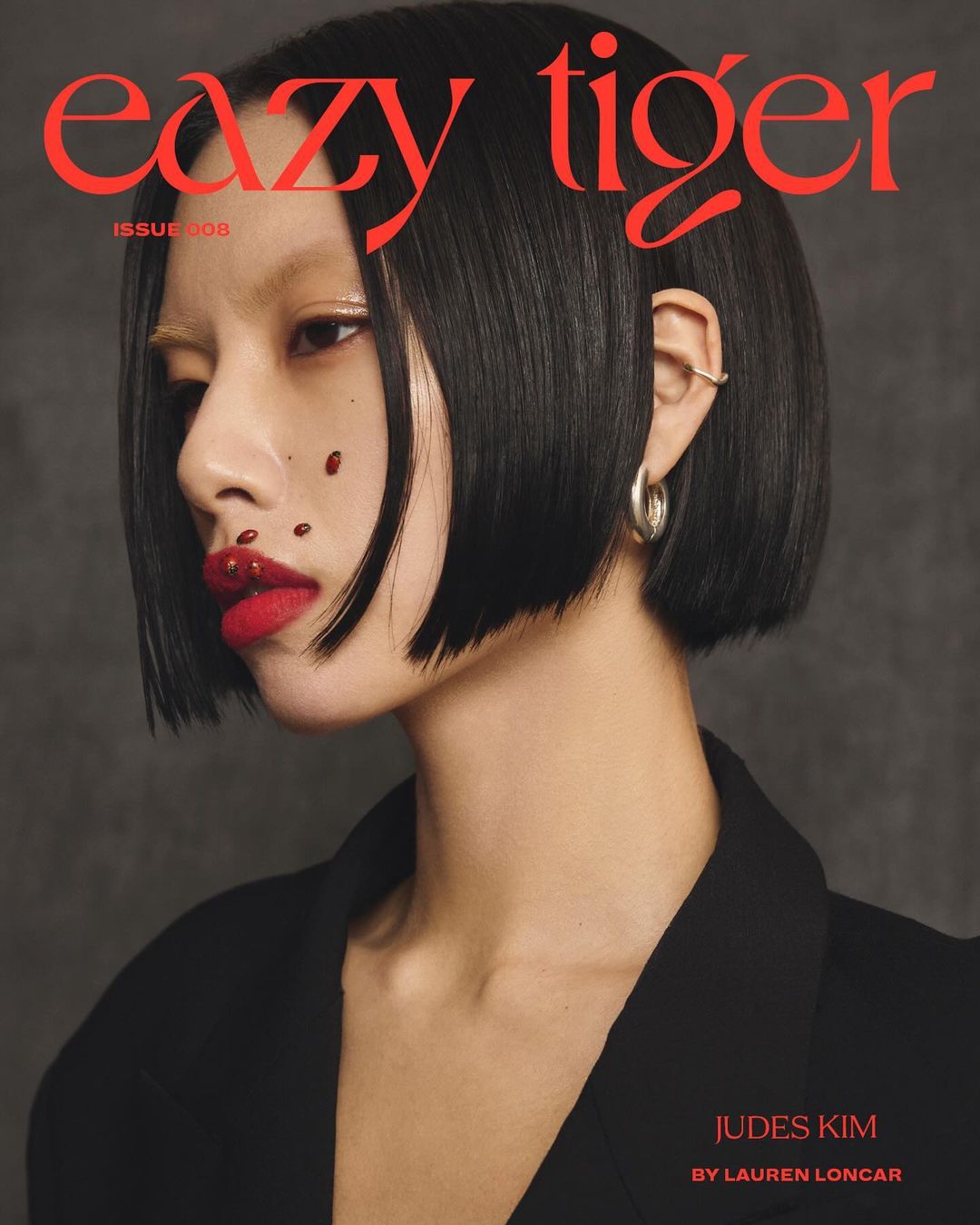 Magazine cover featuring an Asian female model with glossy red lips, black bob haircut, wearing a black blazer against a gray background.
