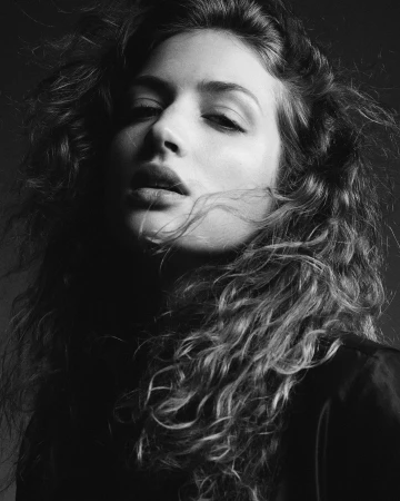 Monochrome portrait of a woman with long curly hair looking down, photographed by Lauren Loncar.