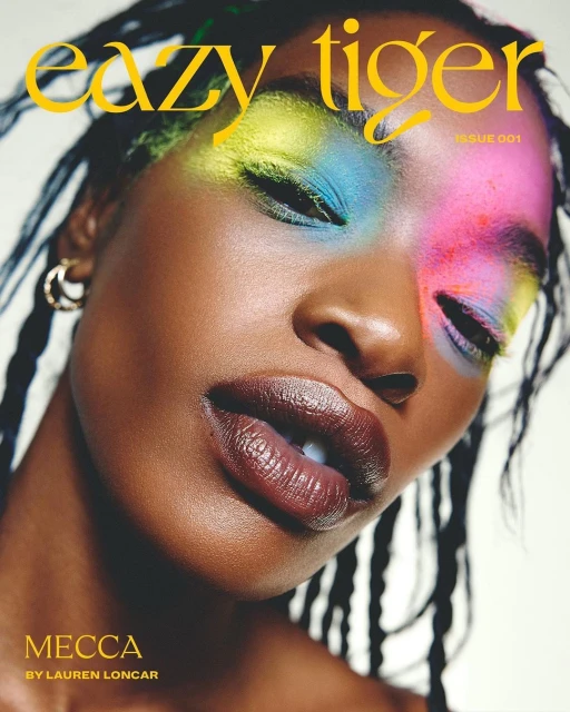 Close-up portrait of a Black woman wearing colorful eyeshadow and glossy lipstick, with braided hair, on a magazine cover.