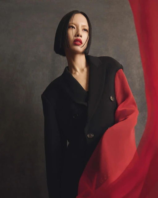 Portrait of a woman with short black hair wearing a two-tone black and red jacket against a dark grey studio backdrop.