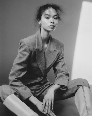 Portrait of a young model wearing a tailored blazer and tall boots seated in a studio by photographer Lauren Maccabee