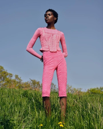 Model in pink patterned two piece outfit standing in a lush green meadow under a clear blue sky