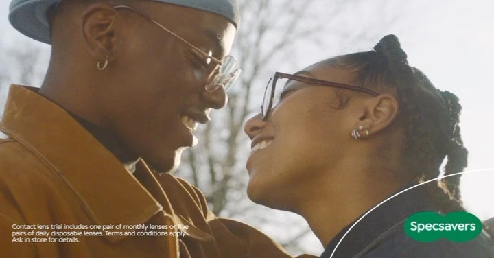 Close-up of an African-American couple in eyeglasses looking at each other and smiling on a sunny day, eyewear ad for Specsavers.
