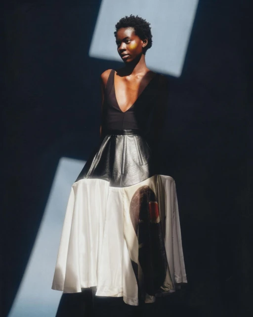 Fashion editorial shot of a black woman in a black top and graphic skirt, posing indoors under artificial light.