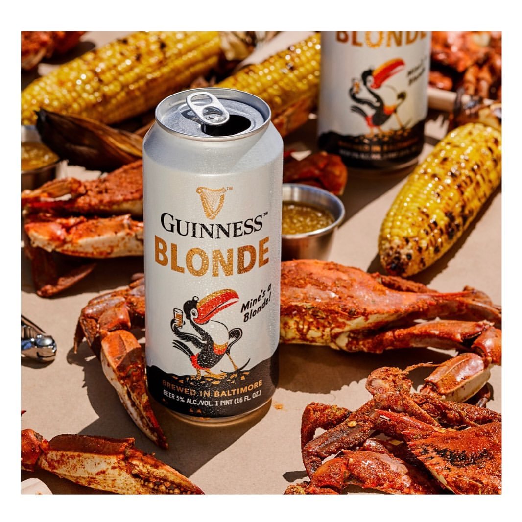 A can of Guinness Blonde beer surrounded by crab legs and grilled corn, creating a visually appealing food and beverage still life.