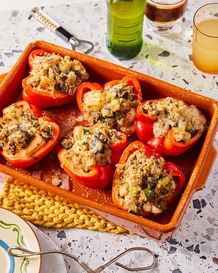 Overhead shot of stuffed red bell peppers in a baking dish with beer and juice glasses on a terrazzo surface. Food photography.
