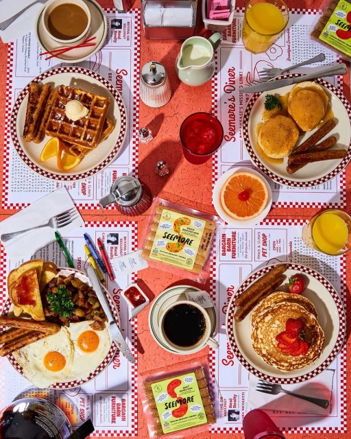 Overhead shot of a diner table filled with plates of waffles, pancakes, eggs, toast, and sausage, with coffee and juice glasses.