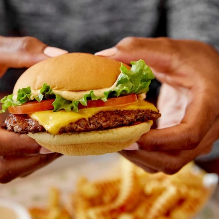 Close-up of a person holding a cheeseburger with lettuce and tomato, photographed by Lauren Volo