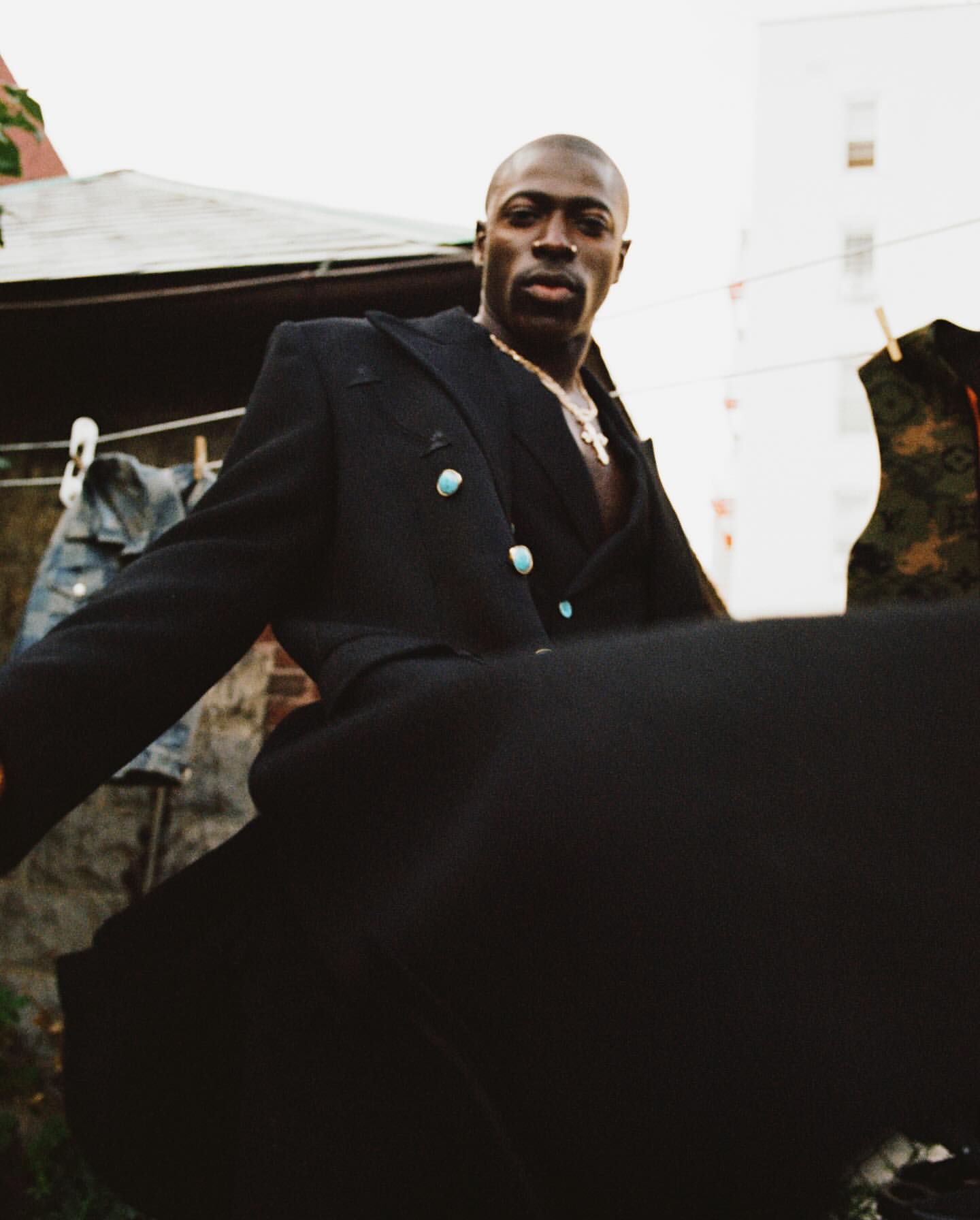 Portrait of an African-American man in a black blazer with turquoise buttons, outdoors in an urban setting on an overcast day.