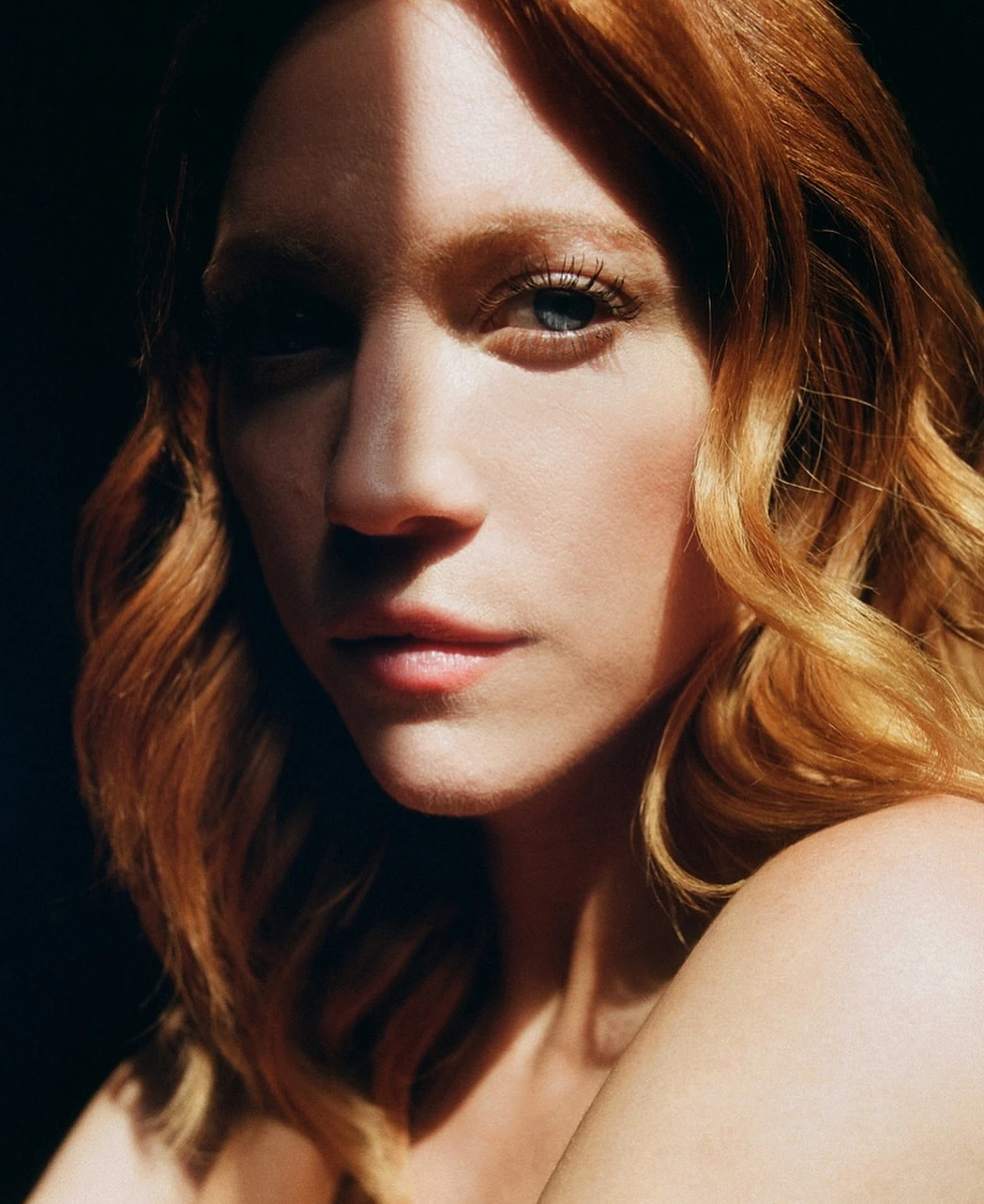 Close-up portrait of a woman with red hair and strong side lighting cutting across her face by photographer Lauren Withrow