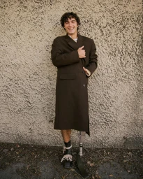 Smiling man in long brown coat posing against a textured stucco wall by photographer Lauren Withrow