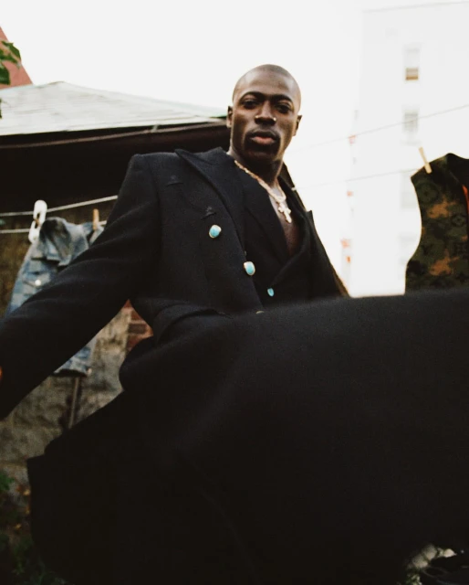 Black man wearing a dark coat with turquoise buttons and a gold chain, photographed outdoors by Lauren Withrow.