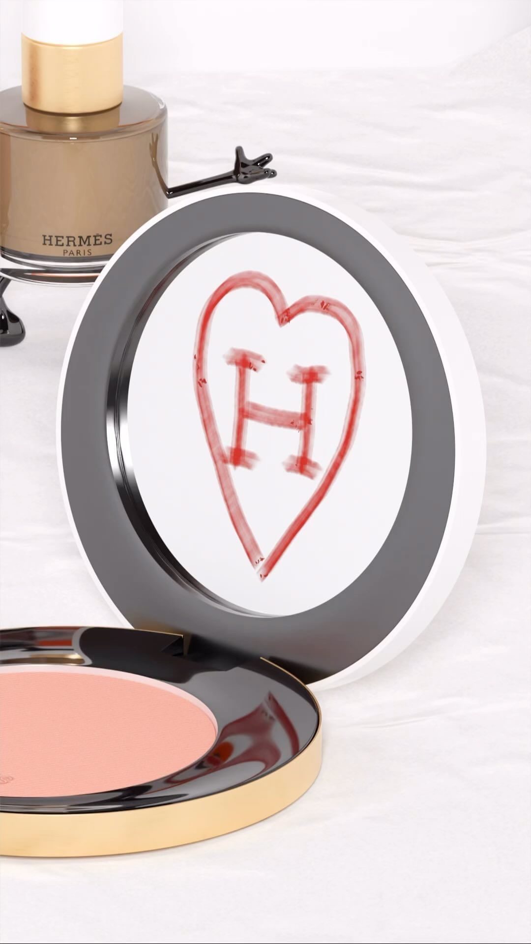 Still life shot of Hermès nail polish and blush compact on a white surface with red heart drawing on a round makeup palette.