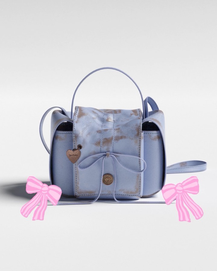 Stylish light blue leather satchel handbag with a handle and shoulder strap, adorned with a decorative bow and a heart charm.