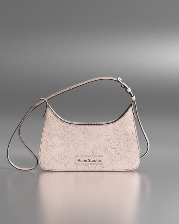 Close-up of a pink Acne Studios handbag with a cracked texture, reflecting light on a gray gradient background in a studio setting.