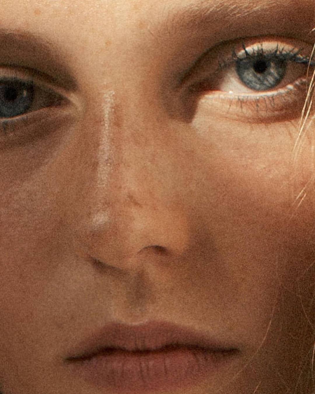 Close-up portrait of a Caucasian woman's face focusing on her blue eyes, nose, and lips, capturing the details of her complexion.