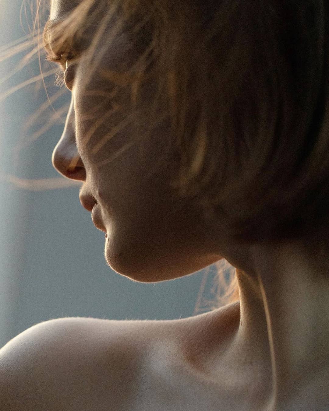 Close-up of a young adult woman's face in profile with shoulder length brown hair; soft, neutral lighting highlights skin and hair.