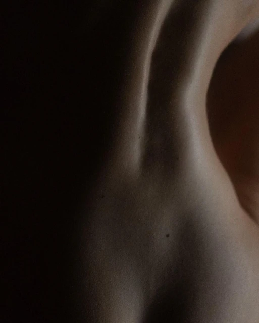 Close-up photograph of the back of an adult, skin detail and musculature. Dramatic lighting highlights the contours of the back.