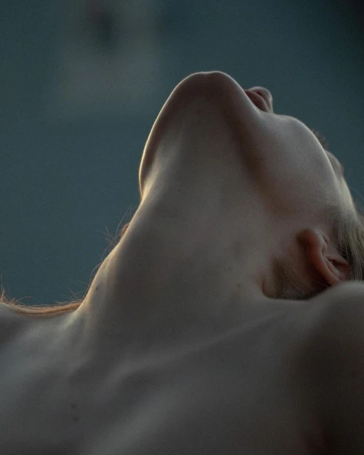 Close-up shot of a fair-skinned adult female lying down with her head tilted back, showcasing her neck and collarbone under natural light.