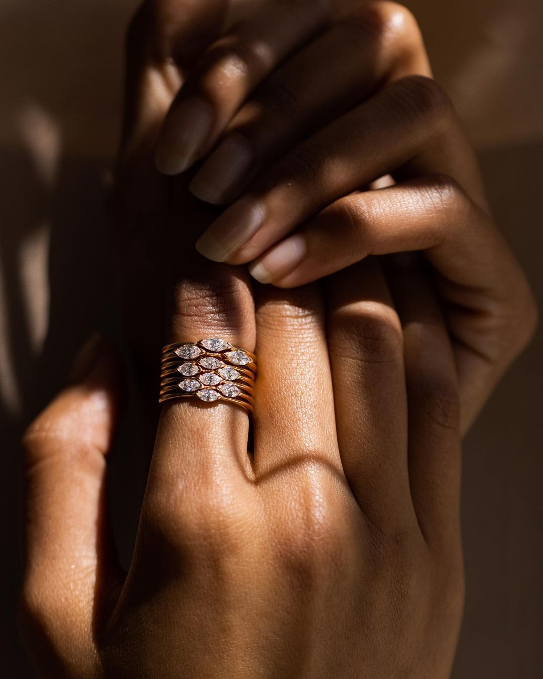 Close-up of woman's hand wearing stacked rose gold and diamond rings, emphasizing jewelry design and elegant style with soft lighting.