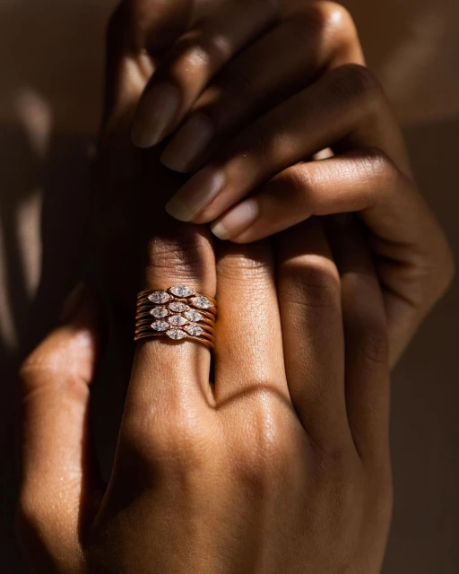 Close-up of woman's hand wearing stacked rose gold and diamond rings, emphasizing jewelry design and elegant style with soft lighting.