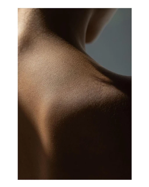 Close-up studio shot of the upper back and shoulder of an adult female, highlighting the texture and contours of the skin in warm lighting.