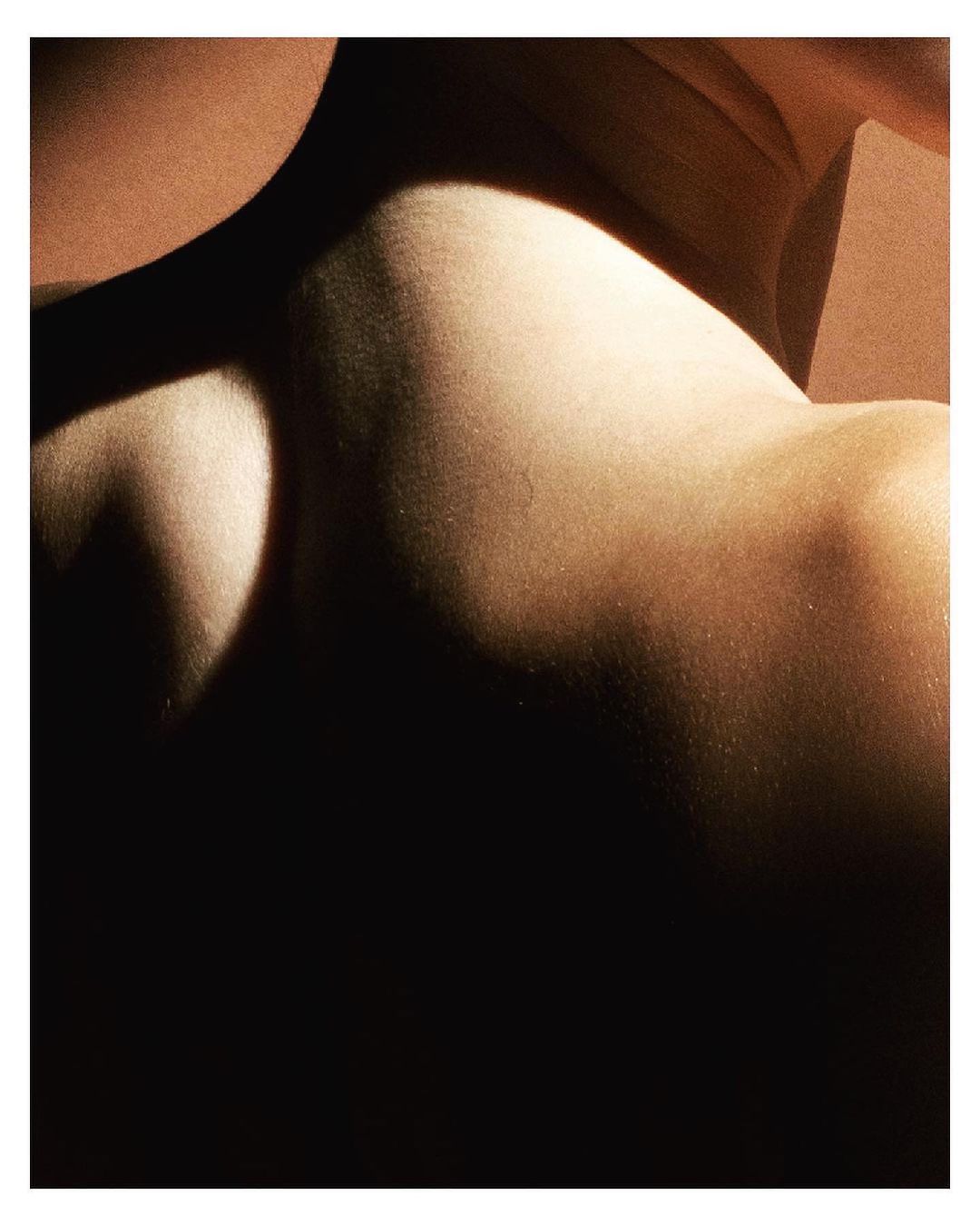 Close-up of an adult human torso, defined by shadows and highlights on the skin, creating an abstract composition of light and dark.