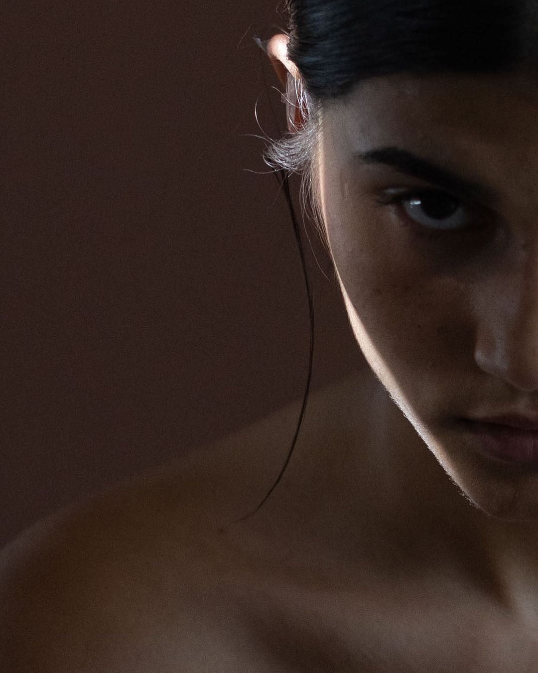 Close-up portrait of a woman with dark hair against a neutral backdrop, showcasing her face with dramatic lighting and soft shadows.