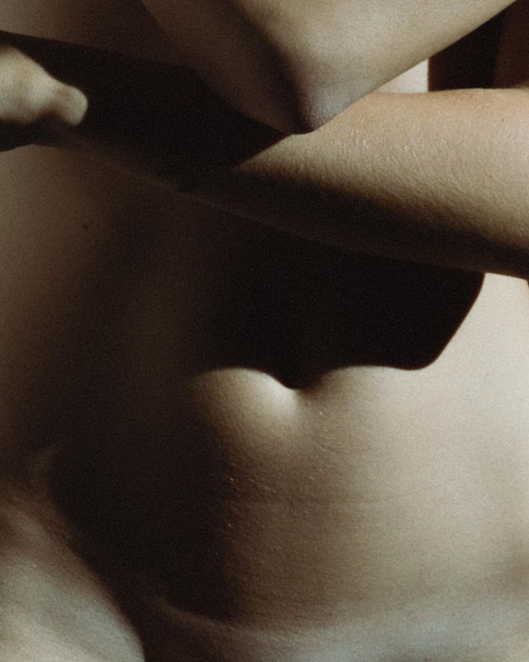 Close-up shot of a person's torso and arm with prominent shadows, showing skin texture and natural body contours.
