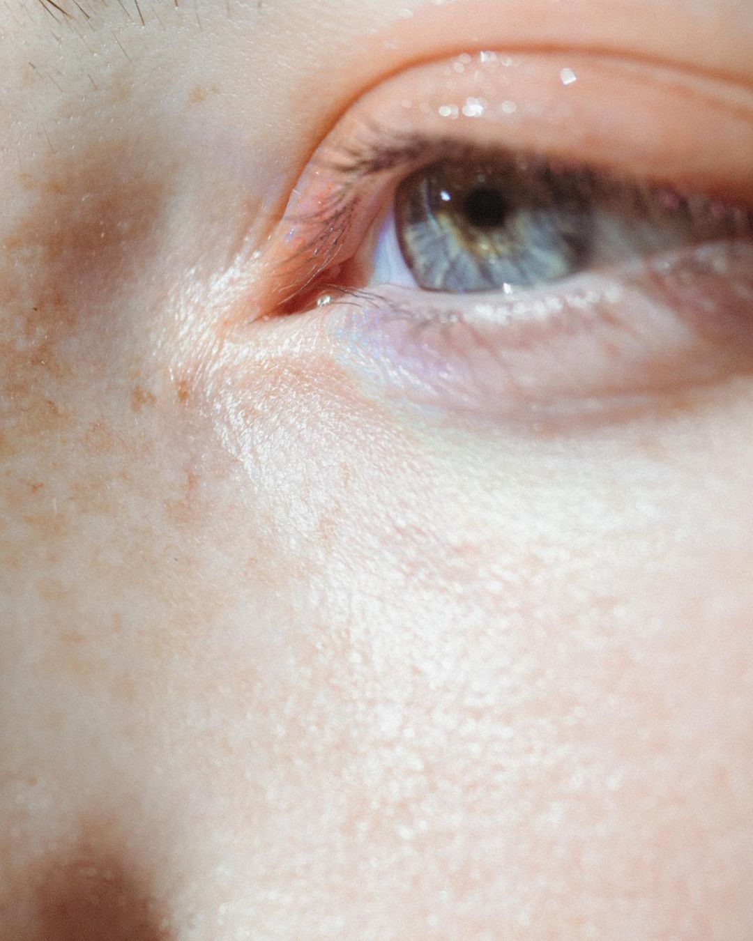 Extreme close-up macro portrait of a blue eye with freckled skin and natural light by Laurent Castellani in Paris.