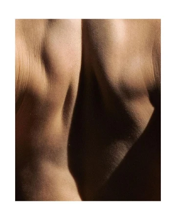 Close-up photograph of a human back, illuminated by natural light casting deep shadows, showing skin texture and definition.