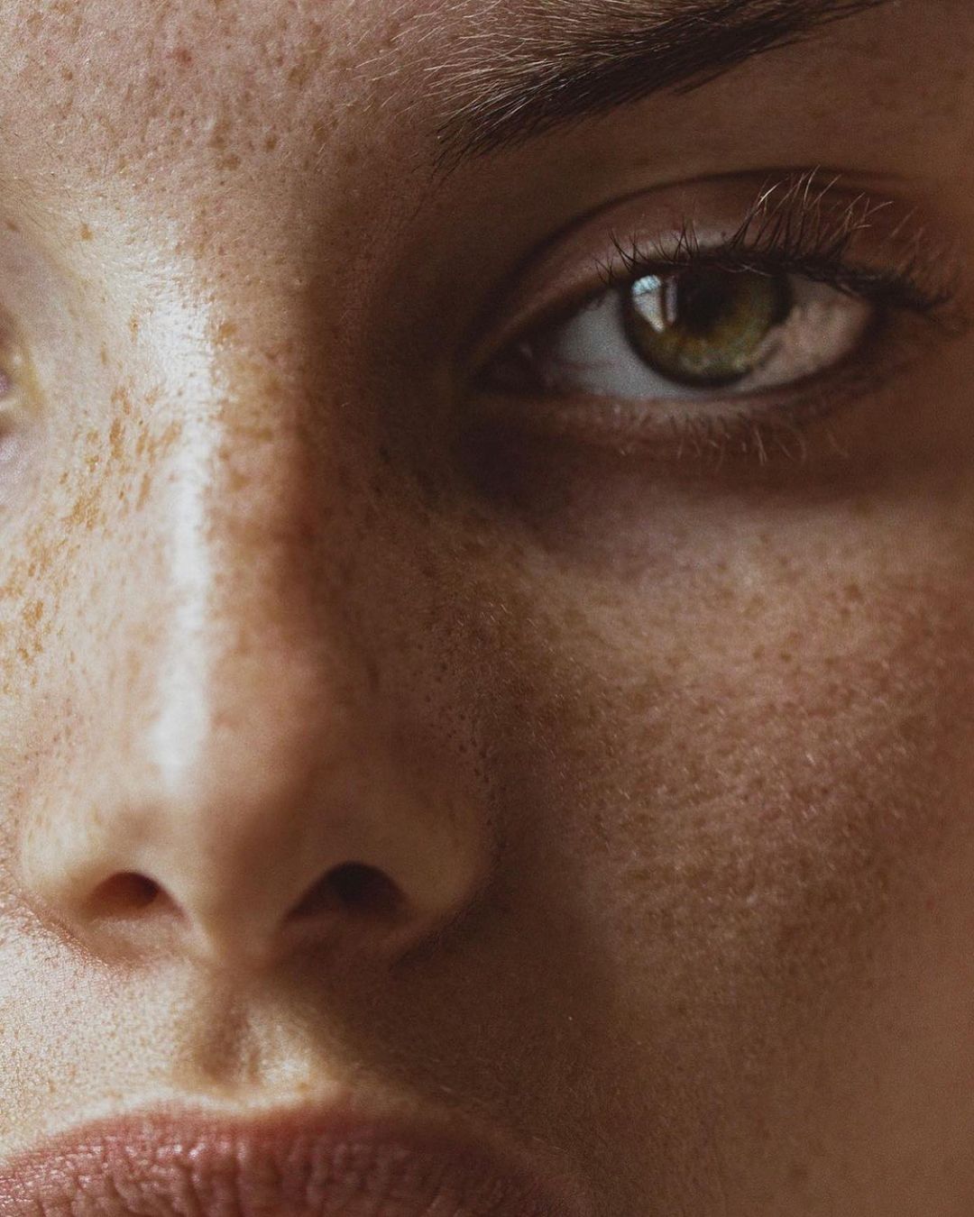 Close-up portrait of a woman's face with light skin, freckles, and a neutral expression, highlighting beauty and detail.