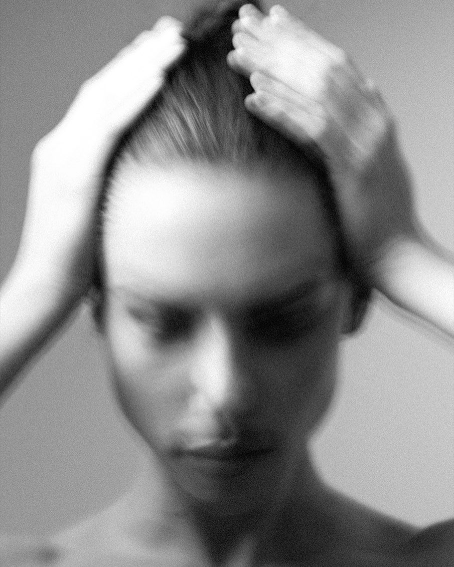 Black and white portrait of a woman with hands on her head, soft focus, and shallow depth of field conveys introspective mood.